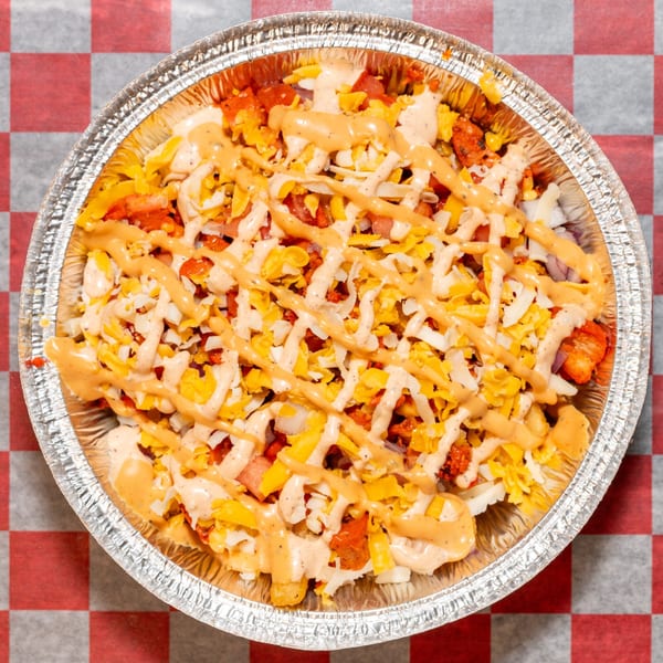 Halal Krush fries topped with chicken, cheese, and two sauces in a foil container.
