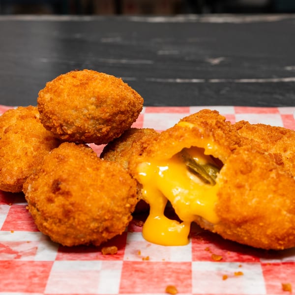Golden-fried jalapeño poppers on red and white checkered paper, one oozing melted cheese.