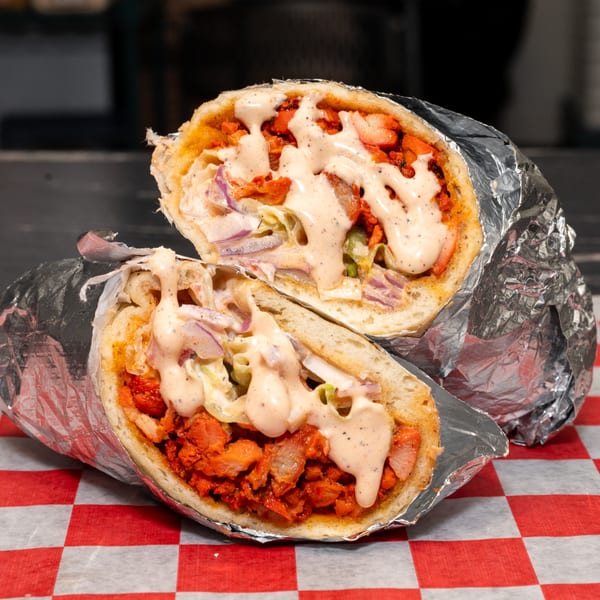 Halal Krush chicken sandwich, cut in half, with sauce and vegetables on checkered paper.