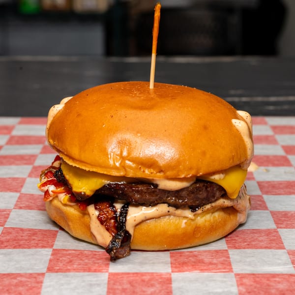 A Halal Krush burger with melted cheese, sauce, and toppings on a red and white checkered paper.