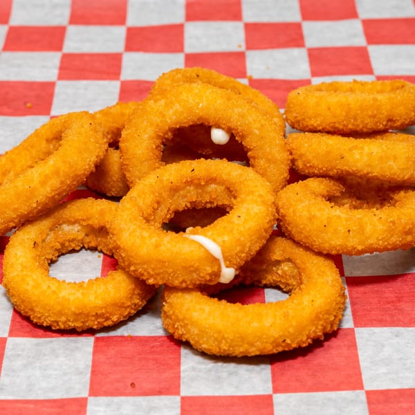 Golden-brown onion rings with melted cheese oozing out, served on red and white checkered paper.